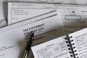 A person reviewing tax forms and documents at a kitchen table with a laptop and notebook