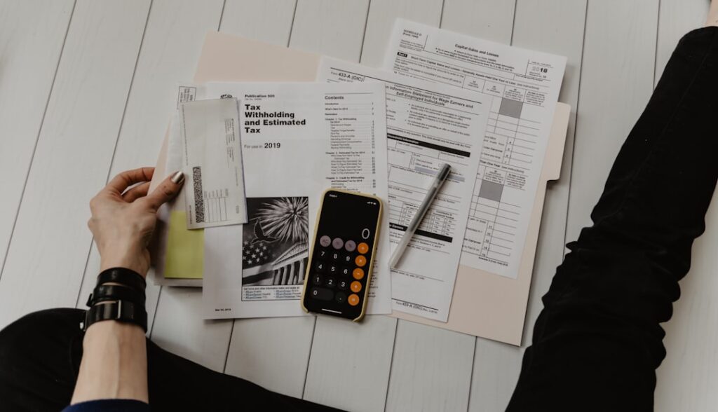 A person sorting tax documents and receipts at a kitchen table, with a calculator and handwritten notes.