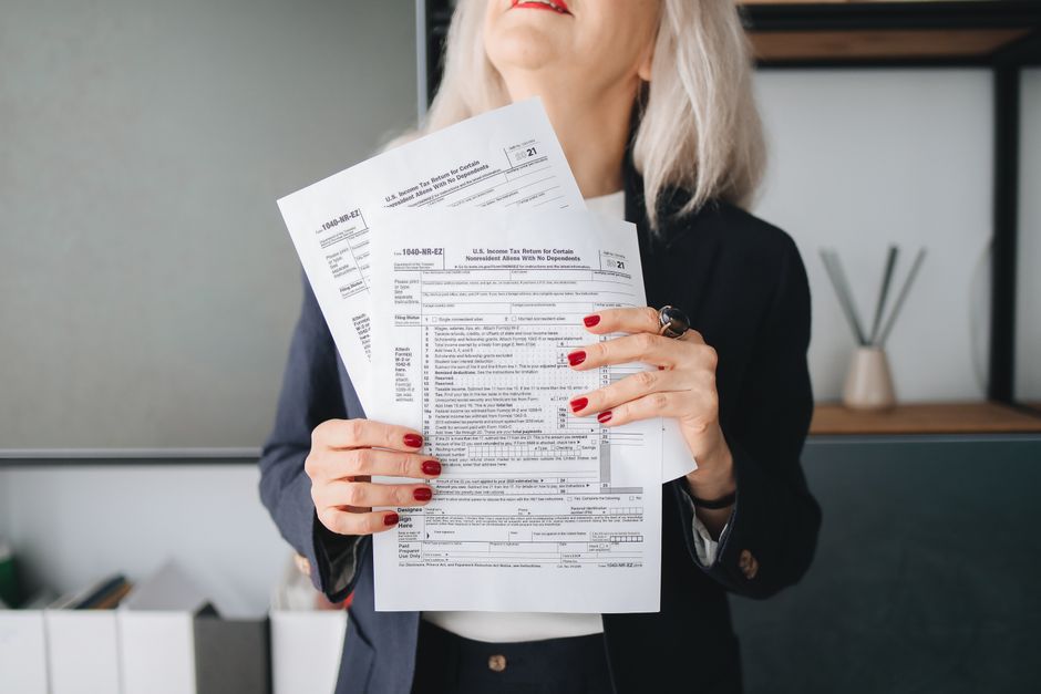 A person reviewing tax documents at a kitchen table with a calculator and laptop.