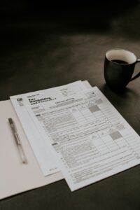 A person reviews paperwork at a kitchen table surrounded by tax forms and financial documents.