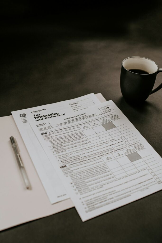 A person reviews paperwork at a kitchen table surrounded by tax forms and financial documents.